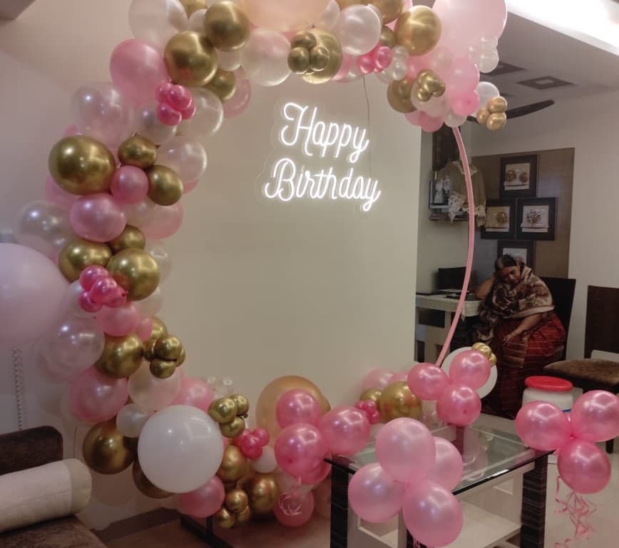 Pink and gold balloon arch with a Happy Birthday neon sign